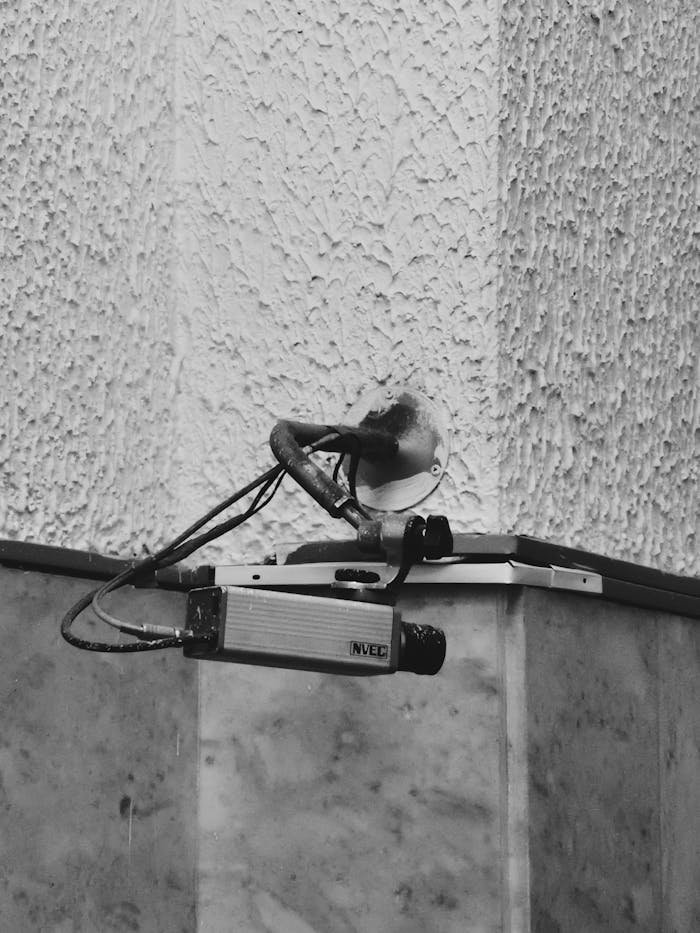 Monochrome image showcasing a surveillance camera mounted on a textured wall.