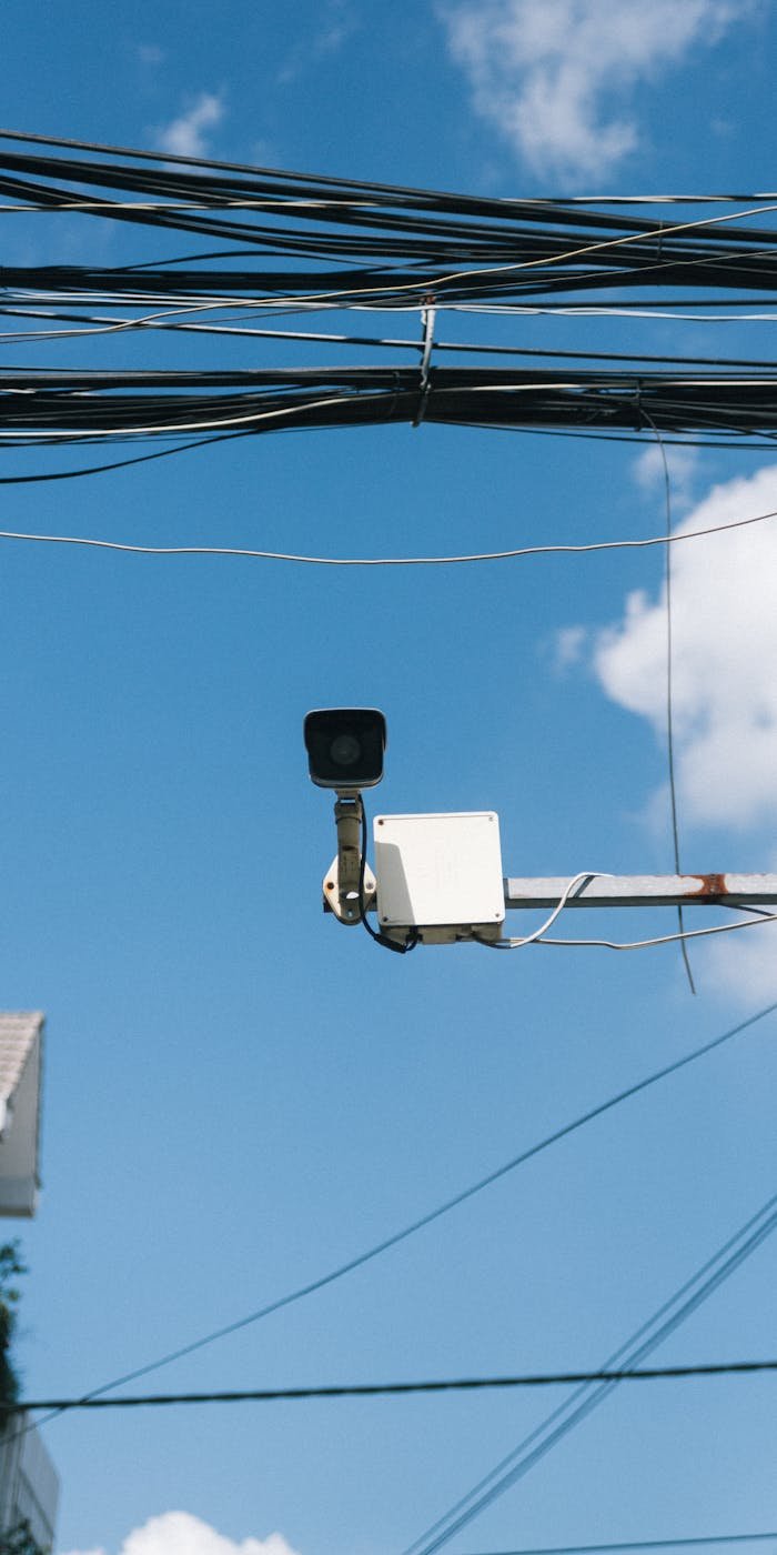 A surveillance camera mounted outdoors under a clear blue sky with power lines.